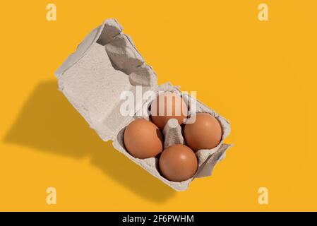 Scatola di uova con uova, quattro uova di pollo in cartone vassoio di uova fatto di carta riciclata isolato su sfondo giallo Foto Stock