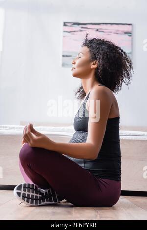 Vista laterale della donna afro-americana incinta seduta in yoga posa Foto Stock