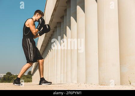 Uomo che pratica e lotta all'esterno, pugile in guanti. Ritratto di pugile maschile Foto Stock