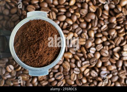 Caffè macinato in un corno tra i chicchi aromatici. Concetto domestico di preparazione del caffè. Orientamento orizzontale. Vista dall'alto. Primo piano. Foto Stock