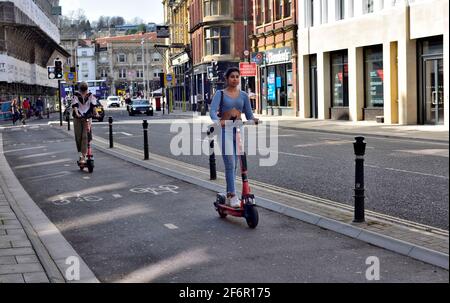 Giovani donne che cavalcano su e-scooter nel centro di Bristol Foto Stock