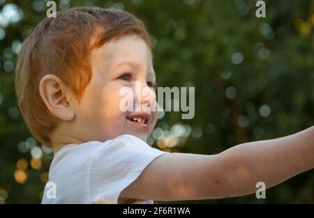 Ritratto di un simpatico ragazzo rosso dagli occhi blu che indossa una t-shirt bianca in un parco giochi in una giornata di sole Foto Stock