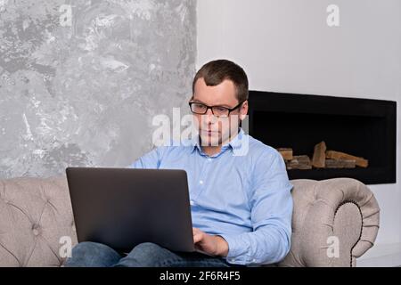 Giovane uomo di successo in una camicia e occhiali lavora con un computer portatile mentre si è seduti in un grande e spazioso ufficio su il lettino sullo sfondo del Foto Stock