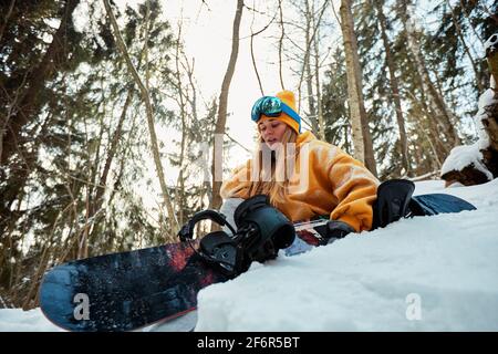 Donna snowboarder in tuta luminosa in un paio di occhiali sportivi tiene una snowboard. Sport estremi. Tempo libero Foto Stock