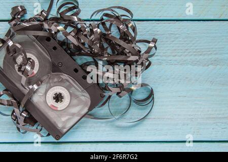 Un nastro audio avvolto in nastro magnetico giace su uno sfondo di legno blu. Spazio vuoto per il testo. Vista dall'alto Foto Stock