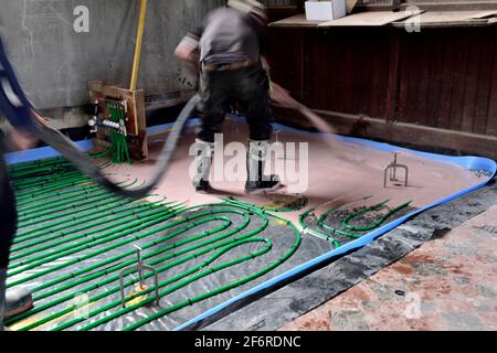 Operatore che versa il rasatore autolivellante con anidrite pompato sopra l'idronico sotto il pavimento tubo di riscaldamento Foto Stock