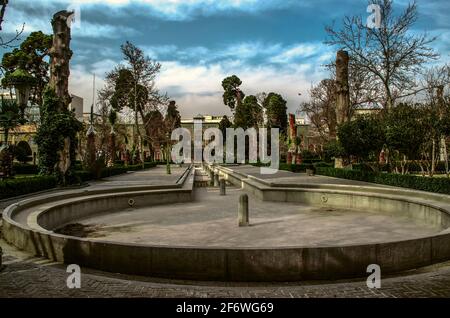 Una piscina circolare con un fossato allungato e 12 fontane lungo un sentiero lastricato in cemento attraverso un vecchio giardino d'inverno Porta all'ingresso del P Foto Stock