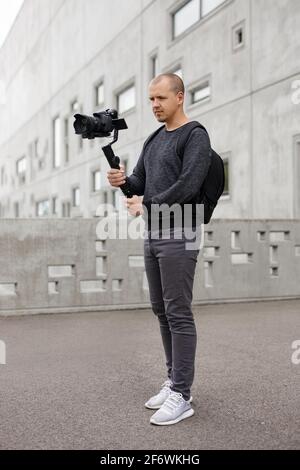 concetto di filmmaking, hobby e creatività - ritratto a tutta lunghezza di un videografo professionista che scatta video utilizzando una moderna fotocamera dslr su un cardanico a 3 assi Foto Stock