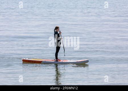 Una solitaria lady paddle boarder in piedi sulla sua tavola Foto Stock