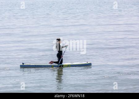 Una solitaria lady paddle boarder inginocchiarsi sulla sua tavola Foto Stock