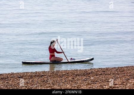 Una solitaria lady paddle boarder inginocchiarsi sulla sua tavola vicino una spiaggia di ciottoli Foto Stock