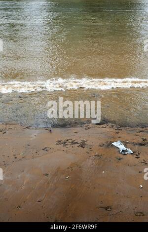 Guardando giù sulla riva del fiume tamigi esposto da basso marea e un'onda di rottura e un singolo pezzo di lettiera spazzatura spazzatura Foto Stock