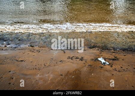 Guardando giù sulla riva del fiume tamigi esposto da basso marea e un'onda di rottura e un singolo pezzo di lettiera spazzatura spazzatura Foto Stock