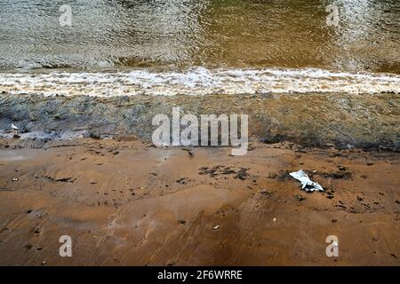 Guardando giù sulla riva del fiume tamigi esposto da basso marea e un'onda di rottura e un singolo pezzo di lettiera spazzatura spazzatura Foto Stock