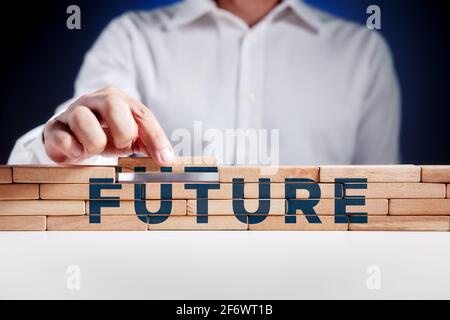 L'uomo d'affari costruisce una struttura di blocchi di legno con la parola futuro. Costruire un concetto futuro. Foto Stock