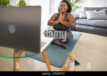 Giovane donna africana che fa yoga lezione di fitness virtuale con computer portatile A casa - e-learning e concetto di stile di vita di benessere delle persone Foto Stock