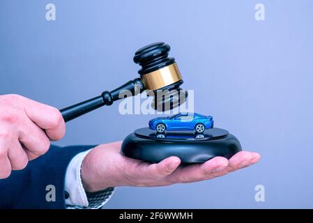 Un uomo che tiene l'auto blu sul gavel del giudice di legno, l'immagine di concetto circa il debito di accreditamento dell'automobile o il divorzio. Foto Stock
