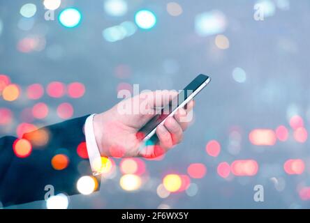 Uomo d'affari che tiene in mano smartphone e sfondo della città con traffico e auto, business concept immagine Foto Stock