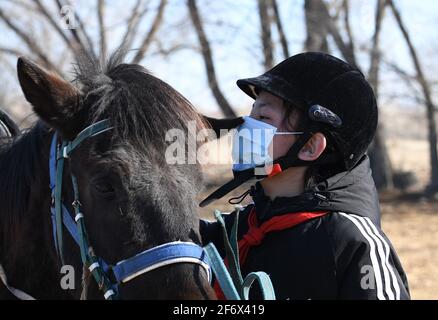 (210403) -- BURQIN, 3 aprile 2021 (Xinhua) -- Marmar Berik, un allievo di grado senventesimo della scuola di imbarco di Oymak, bacia un cavallo durante una classe equestre nella contea di Burqin, regione autonoma di Xinjiang Uygur, 30 marzo 2021. La gente nella regione autonoma di Xinjiang Uygur ha una tradizione di allevamento di cavalli e di equitazione. La scuola di imbarco di Oymak ha cominciato ad offrire le classi equestri alla fine del 2019. Gli studenti, la maggior parte dei quali provengono da famiglie di pastori, imparano sia la conoscenza teorica che la pratica di equitazione sulle classi equestri. Dopo le lezioni, gli studenti si rafforzano fisicamente e amano Foto Stock