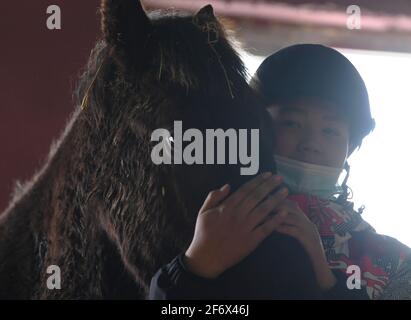 (210403) -- BURQIN, 3 aprile 2021 (Xinhua) -- Parasat Zhumabek, uno studente di grado senventesimo della Oymak Boarding School, tocca un cavallo durante una classe equestre nella contea di Burqin, nella regione autonoma di Xinjiang Uygur, 29 marzo 2021. La gente nella regione autonoma di Xinjiang Uygur ha una tradizione di allevamento di cavalli e di equitazione. La scuola di imbarco di Oymak ha cominciato ad offrire le classi equestri alla fine del 2019. Gli studenti, la maggior parte dei quali provengono da famiglie di pastori, imparano sia la conoscenza teorica che la pratica di equitazione sulle classi equestri. Dopo le lezioni, gli studenti si rafforzano fisicamente e lo Foto Stock