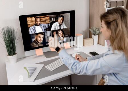 Vista posteriore di una bella dipendente femminile di stile che mostra i pollici ai colleghi durante la riunione online. Elegante donna d'affari in abbigliamento formale da lavoro Foto Stock