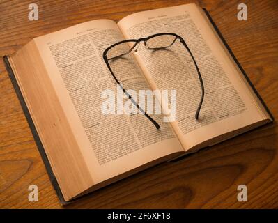 Gli occhiali giacciono su un libro aperto che è più di 100 anni Foto Stock