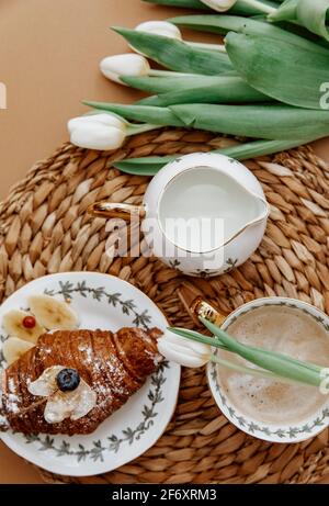 Croissant e una tazza di caffè su un tavolo con tulipani Foto Stock