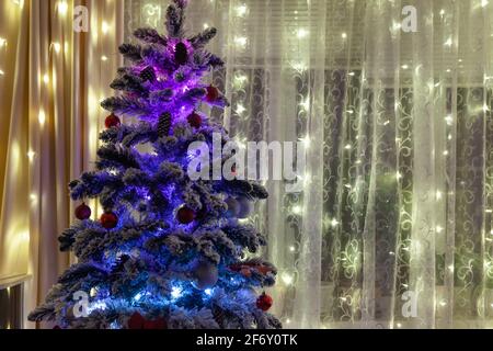 Albero di Natale con ghirlanda contro le tende, utilizzato come sfondo Foto Stock