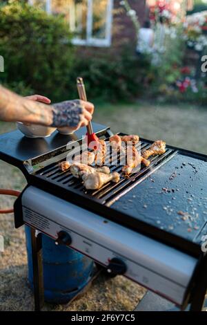 Primo piano di un uomo che inforna ali di pollo con le ali fatte in casa salsa barbecue su un barbecue a gas Foto Stock
