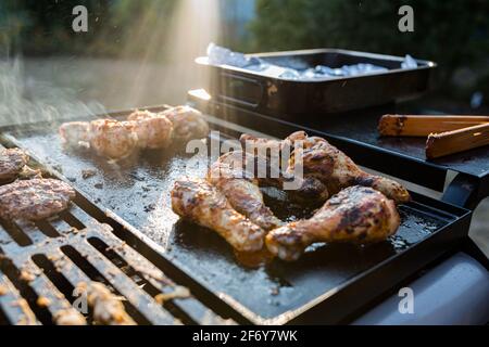 Primo piano di una griglia barbecue con carne che cucinano su di loro, luce solare sullo sfondo sta catturando il fumo Foto Stock