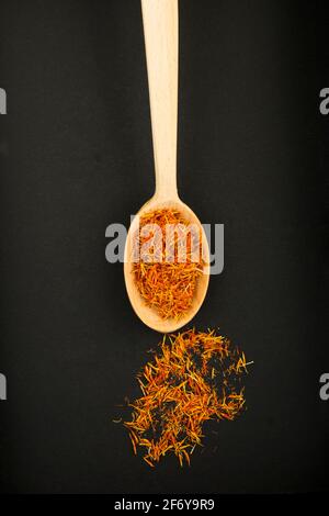 Vista dall'alto dello zafferano asciutto nel cucchiaio di legno sullo sfondo scuro. Posizione verticale. Foto Stock