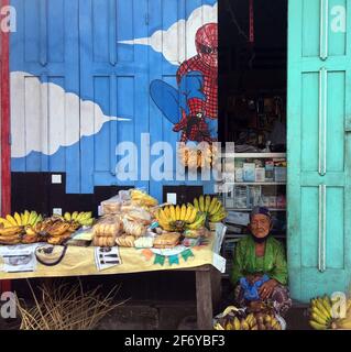 Yogyakarta, Indonesia - 2 aprile 2021: Una donna anziana che vende banane sotto un manifesto dello spiderman, in via Bantul, Regione Speciale di Yogyakarta, Indonesia Foto Stock