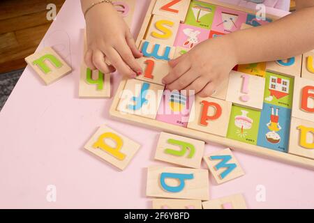 Ragazza di quattro anni che gioca con closeup puzzle alfabeto in legno delle sue mani al lavoro tra le lettere colorate Foto Stock