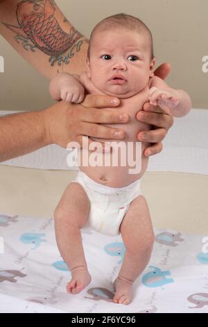 Neonato bambino di 7 settimane tenuto in posizione eretta con peso su suole di piedi, neonato riflesso passo Foto Stock