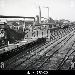 Anni '50, vista storica di una ferrovia industriale e dei treni merci che servono un grande stabilimento di produzione, Inghilterra, Regno Unito. Tali ferrovie erano un tempo un sito comune in Gran Bretagna, con treni merci che trasportavano materie prime pesanti e alla rinfusa lungo una pista verso altre parti del complesso. La crescita del trasporto su strada e i cambiamenti nella produzione hanno visto la rapida diminuzione dei binari e dei binari ferroviari industriali. Foto Stock