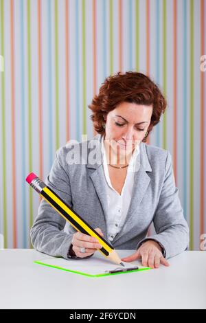 Donna d'affari che scrive con una matita gigante al suo ufficio Foto Stock