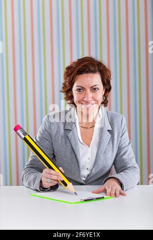 Donna d'affari che scrive con una matita gigante al suo ufficio Foto Stock