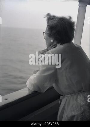 1956, storica, una donna in un arcobaleno e sciarpa da collo, in piedi sul lato di una barca che pende sul taffrail o corrimano che guarda verso il mare, sulla costa vicino a Bridlington, East Yorkshire, Inghilterra, UK. Guardare fuori al blankness dell'oceano è spesso un tempo per il pensiero profondo o per i momenti di contemplazione Foto Stock