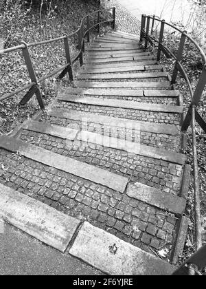 Scale storiche curvate che guardano al piano inferiore con corrimano in metallo, motivi in ciottoli e struttura su un'immagine verticale in bianco e nero Foto Stock