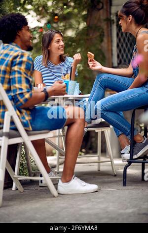 Amici allegri che hanno uno spuntino nel cortile del bar in un bel tempo. Tempo di amicizia di qualità insieme Foto Stock