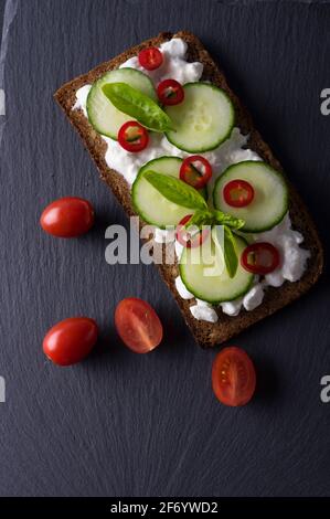 Sandwich di primavera fresco su un pane di girasole senza glutine a fette. Verdure rosse e verdi su pietra ardesia nera. Cetriolo, peperoncino e garni di formaggio cottage Foto Stock