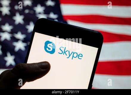 In questa illustrazione è illustrato il software applicativo per le telecomunicazioni per le chat video e le chiamate vocali il logo Skype visualizzato su uno smartphone con una bandiera degli Stati Uniti sullo sfondo. Foto Stock
