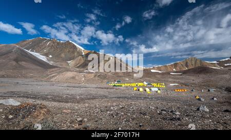 Achik Tash base Camp sul picco di Lenin, Pamir montagne, Kirghizistan, con cielo blu e tende da campeggio giallo Foto Stock