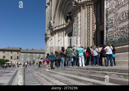 I turisti si ergono sui gradini di fronte alla cattedrale, si può ottenere una spiegazione del rilievo sulle mura ed entrare nel Duomo di Orvieto Foto Stock