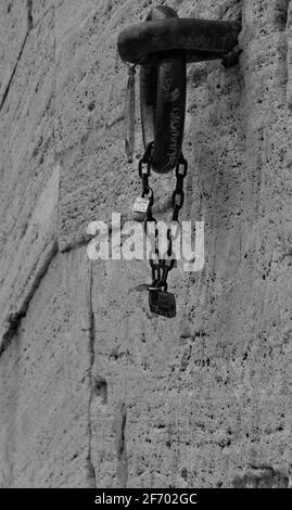Particolare di una catena bloccata con lucchetti appesi ad un anello di ferro in un muro di pietra Foto Stock