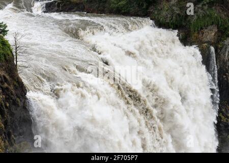 L'acqua si tuffa con forza estrema sul bordo del Cascata Snoqualmie Falls durante un'inondazione che crea strati di texture tra le pareti rocciose Foto Stock