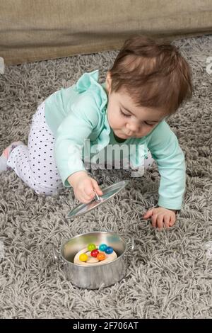 10 mese bambina ragazza bambino aprire coperchio su pentola a. Trova il giocattolo nascosto Piaget permanenza oggetto Foto Stock