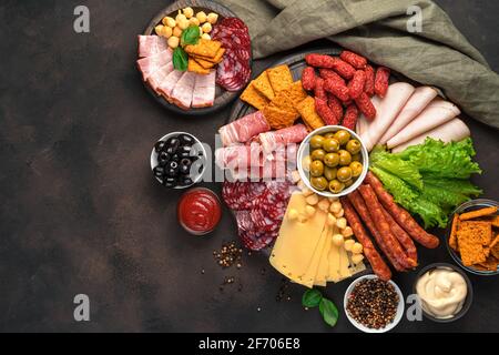 Prelibatezze di carne, salumi, salsicce di vario tipo, olive e salse su tavola marrone. Spuntini affumicati. Sfondo culinario, spazio di copia. Foto Stock