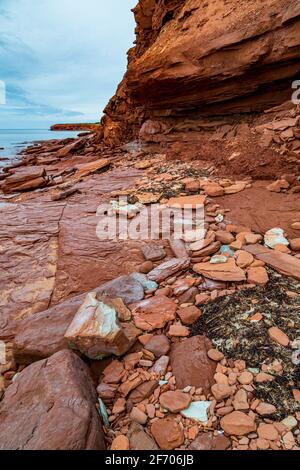 Sulla spiaggia di Cavendish, sull'isola del Principe Edoardo del Canada, la pietra arenaria piatta rossa e turchese è coperta da rocce cadute causate dall'erosione Foto Stock