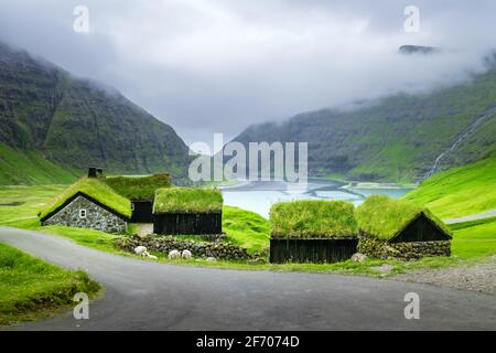 Paesaggio di bellezza con case erbose e alte montagne vicino alla famosa chiesa Saksunar Kirkja nel villaggio di Saksun. Isola di Streymoy, Isole Faroe, Danimarca. Foto Stock